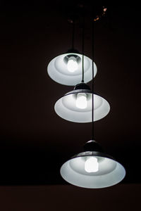 Low angle view of illuminated pendant lights hanging against black background
