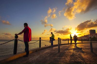 People standing on beach against sky during sunset