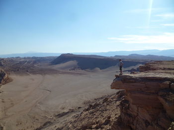 Mid distance view of man standing on cliff at desert during sunny day