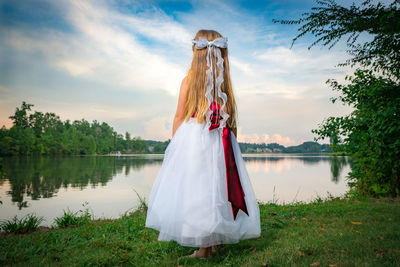 Rear view of girl standing at lakeshore during sunset