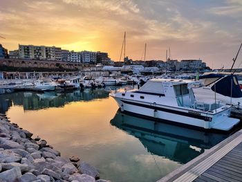 Boats moored in harbor at sunset