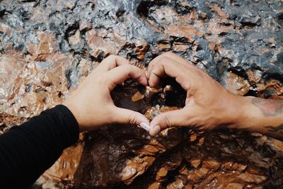 Cropped image of couple making heart shape with hands by rock