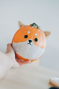 Close-up of hand holding pumpkin against orange background