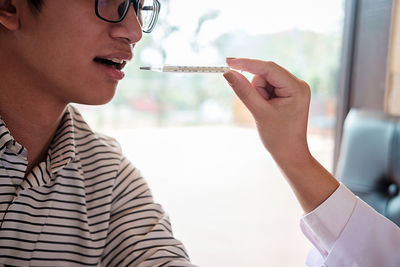 Cropped hand of doctor putting thermometer in patient mouth