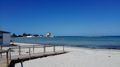 Boardwalk on sand at beach against clear sky