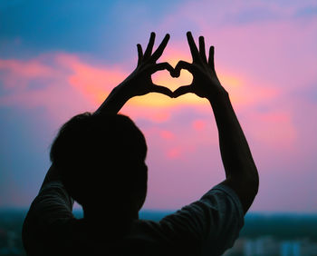 Rear view of silhouette woman with heart shape against sky during sunset