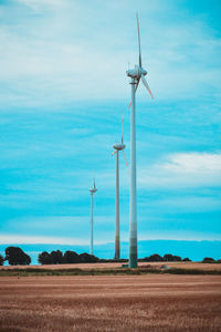 Low angle view of wind turbines on field against sky