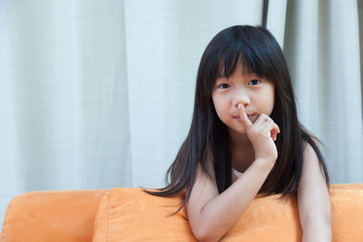 Portrait of girl with finger on lips sitting on sofa at home