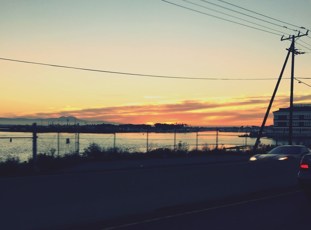 sunset, transportation, power line, silhouette, orange color, electricity pylon, mode of transport, sky, road, car, cable, connection, street light, land vehicle, scenics, water, nature, dusk, electricity, no people