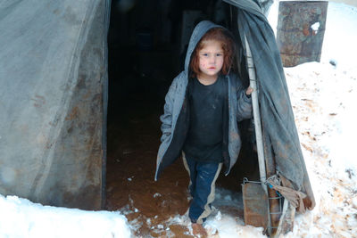 A syrian refugee child at the door of his snow covered tent.