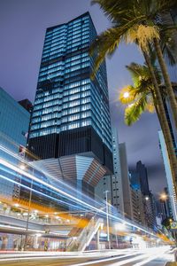 Light trails on city street by buildings against sky