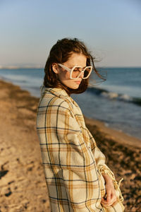 Portrait of young woman wearing sunglasses standing at beach