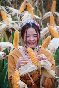 Smiling woman holding corn while standing on field