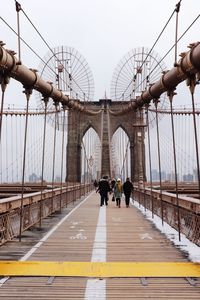 People walking on bridge in city against sky