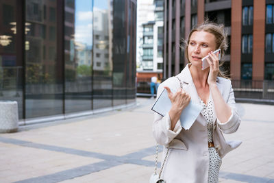 A beautiful blonde girl holds a smartphone and a notebook in her hands.