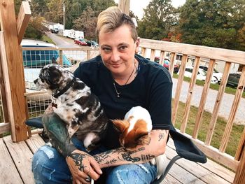 Woman holding cat and dog sitting on chair at balcony