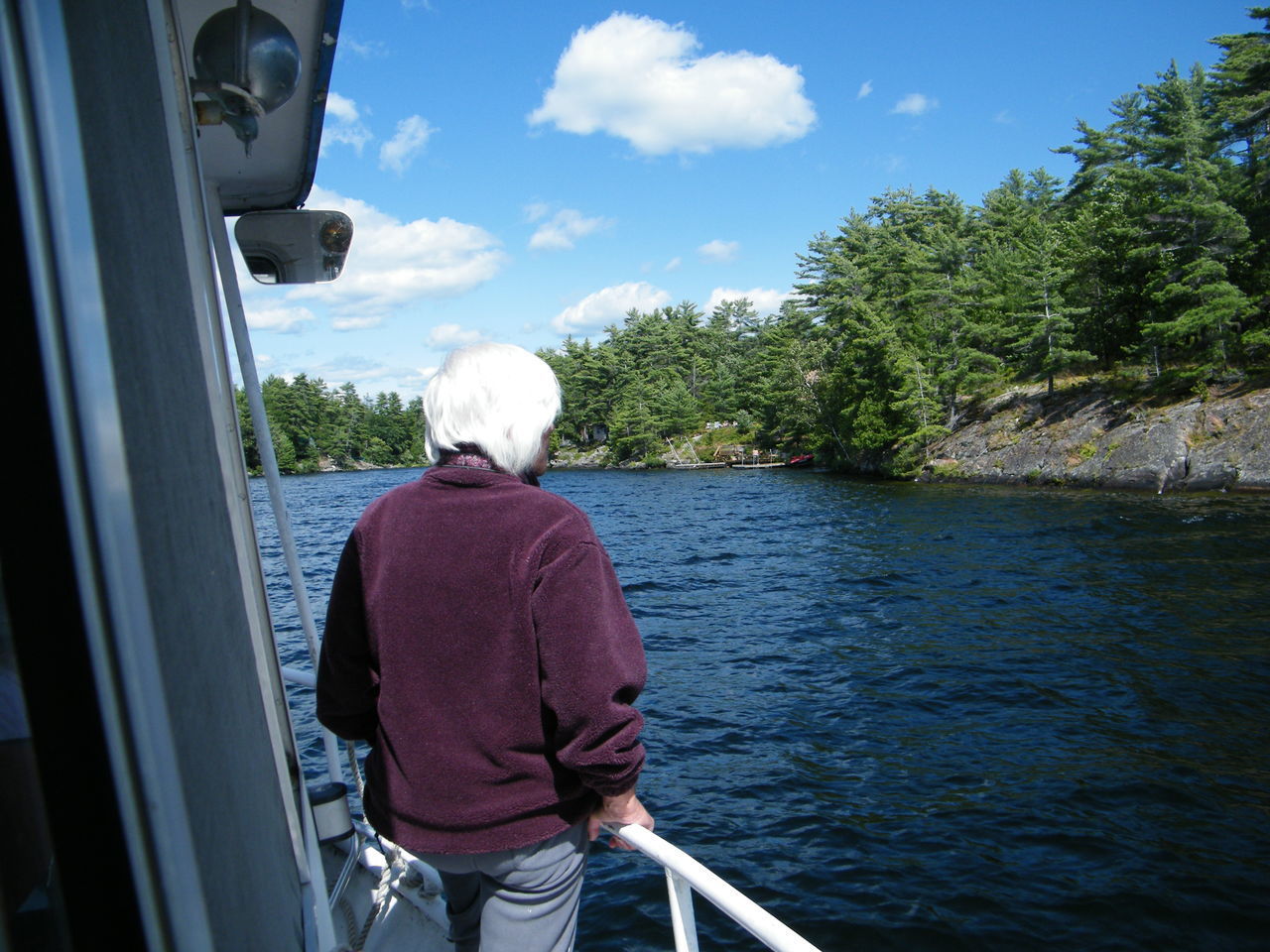 REAR VIEW OF MAN STANDING IN BOAT AGAINST SKY