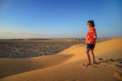 Rear view of woman walking on sand at desert against clear sky