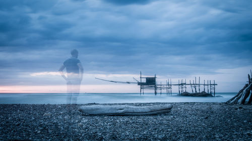 Double exposure of man standing on shore against cloudy sky during sunset