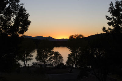 Silhouette trees by calm lake at sunset