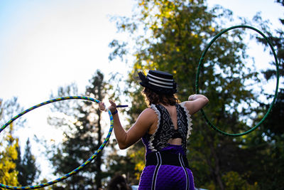 Rear view of woman holding plant against trees