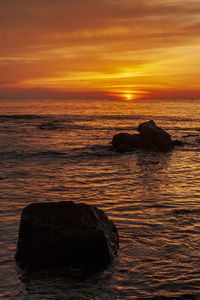 Rock formation in sea against sky during sunset