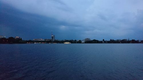 View of city at waterfront against cloudy sky