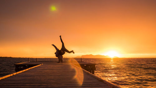 Man doing headstand on pier over sea against clear sky during sunset