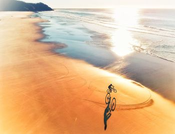 Boy riding bicycle on beach during sunset