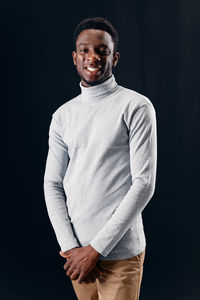 Portrait of young man standing against black background