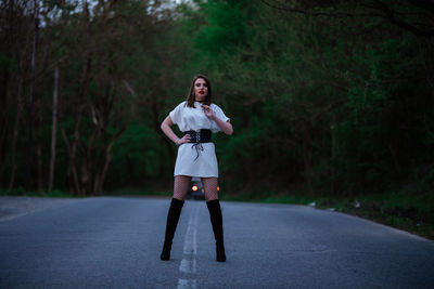 Full length portrait of young woman standing on road in forest