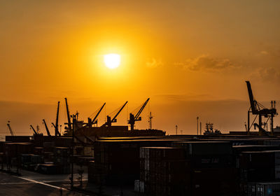 Silhouette cranes at construction site against sky during sunset