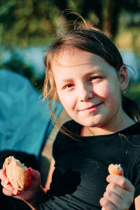 Portrait of cute girl holding food sitting outdoors