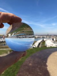 Close-up of hand holding crystal ball against blue sky