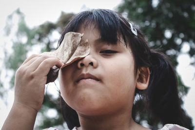 Portrait of girl holding leaf over eye against tree