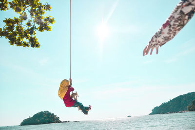 Low angle view of girl on rope swing over ocean