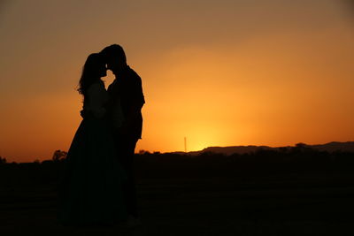 Silhouette couple standing against orange sky during sunset