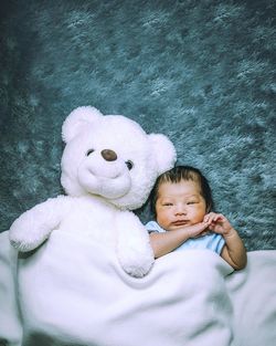 High angle portrait of cute baby boy with stuffed toy lying down on bed