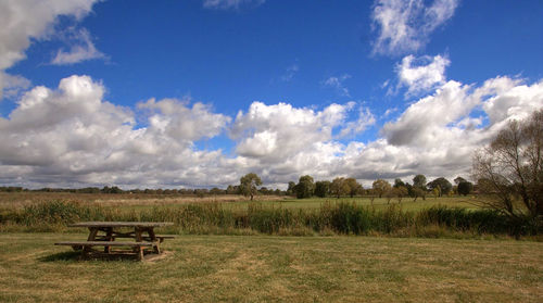 Empty bench on field against sky