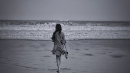 Rear view of woman standing at beach against sky