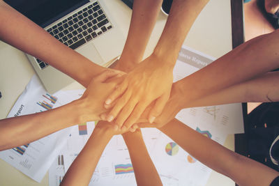 Cropped image of business people stacking hands over documents in office