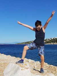 Boy standing on shore at beach against clear blue sky