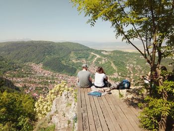 Rear view of man and woman sitting on observation point against sky