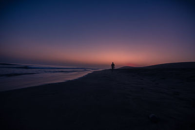 Silhouette man standing on beach against sky during sunset