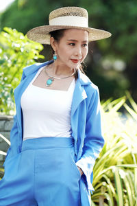 Young woman wearing hat standing against plants