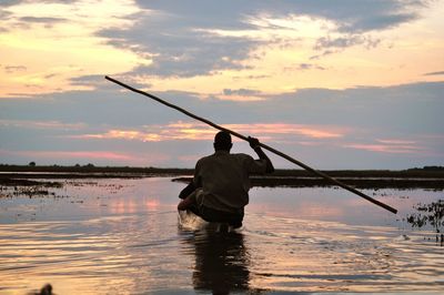 Silhouette fisherman rowing boat with bamboo in lake during sunset