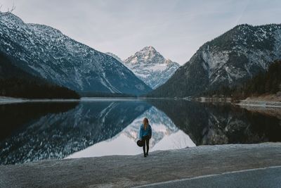 Man standing on snowcapped mountain by lake against sky