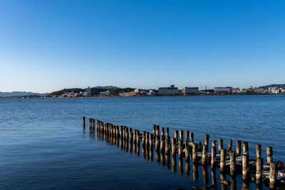 Wooden posts in sea against clear blue sky