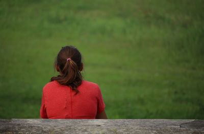 Rear view of woman sitting on bench over grassy field