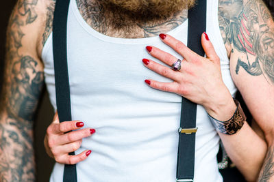 Midsection of a man holding in shirt with beard and suspenders and female hands